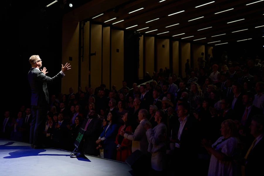 A speaker on a spotlighted stage with an attentive audience